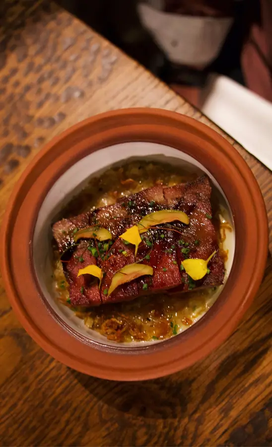 Glazed sliced meat with yellow petals and chives in a terracotta bowl