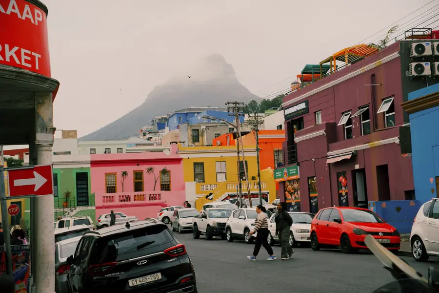 A Bo-Kaap street of pink, yellow and green houses below a cloud-capped peak