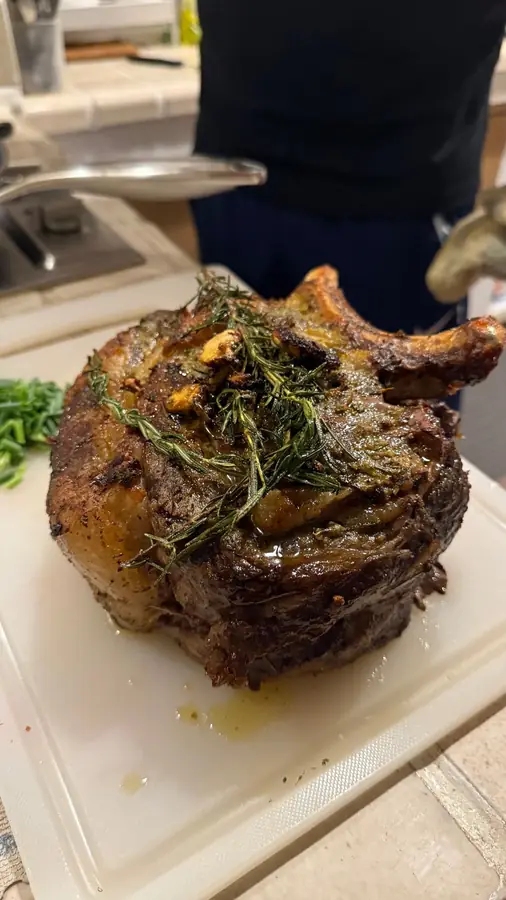 A bone-in rib roast topped with rosemary and garlic on a white cutting board