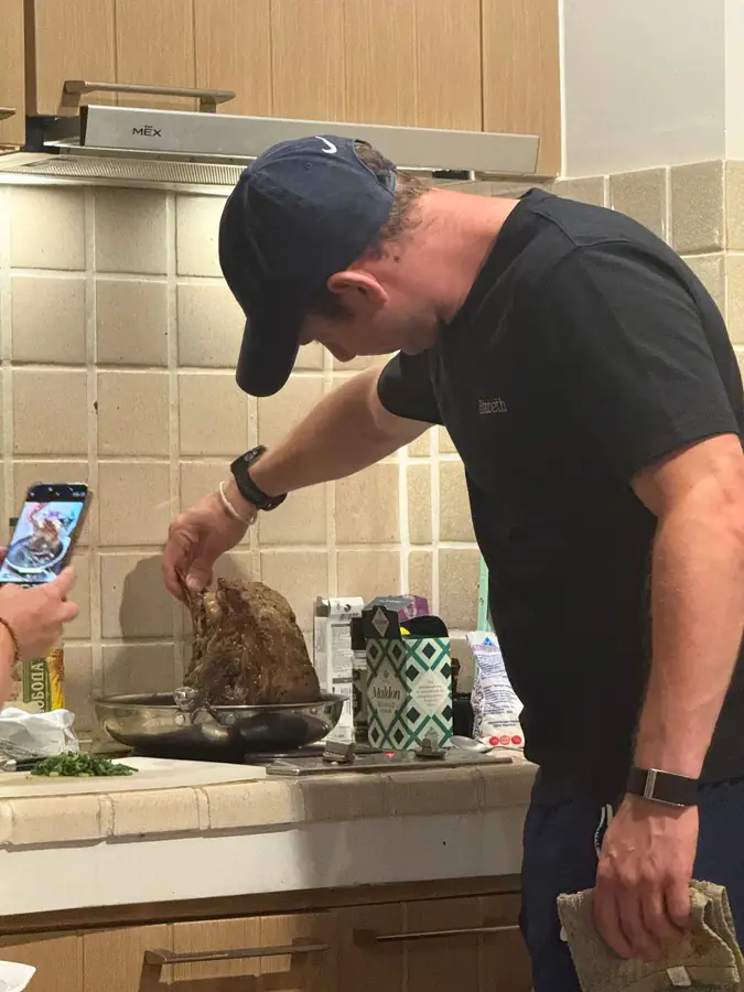 Jason in a black t-shirt and cap checks a rib roast in a pan