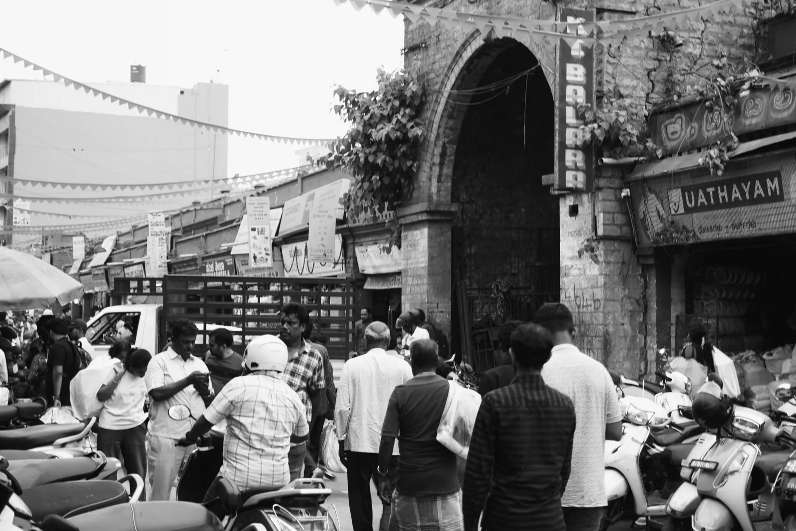 A black-and-white photograph of shoppers and scooters on a busy Bengaluru street