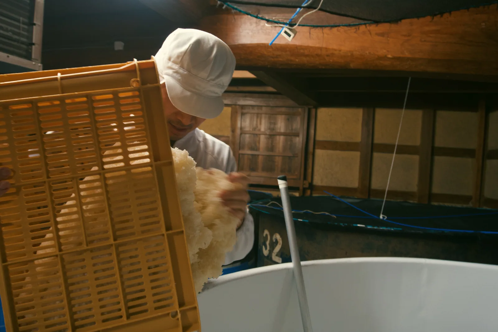 A brewery worker emptying a wooden tray of rice into a vessel