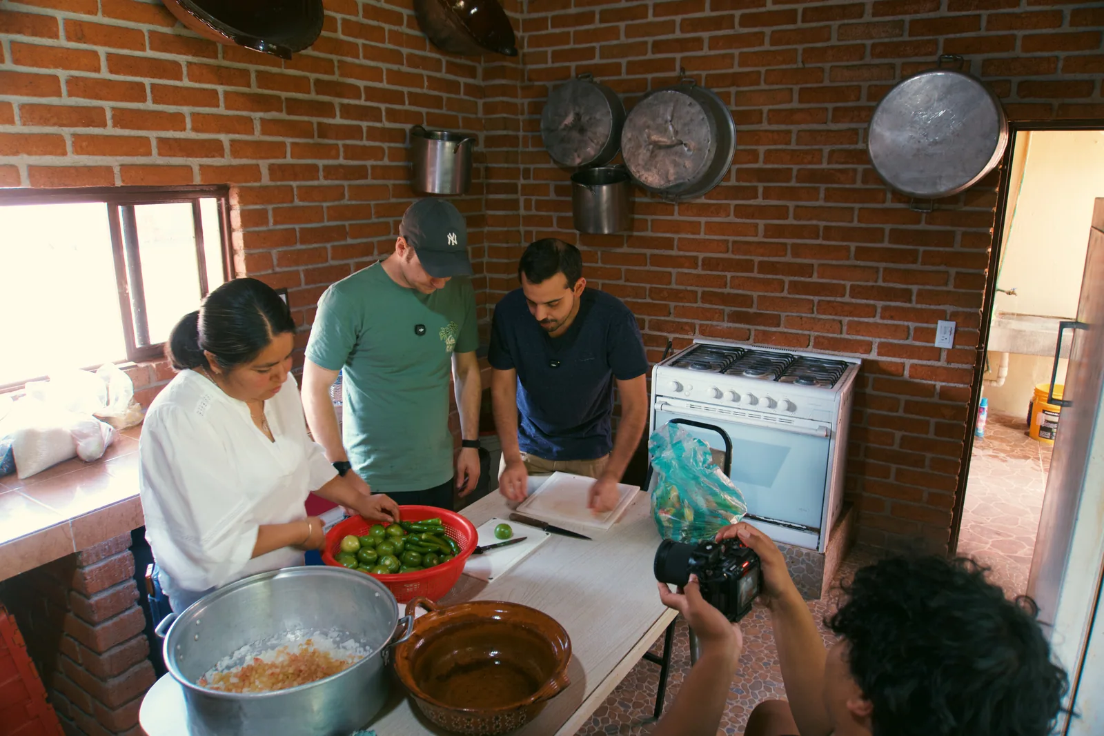 Jason and Travis watching a woman prepare ingredients in a family kitchen