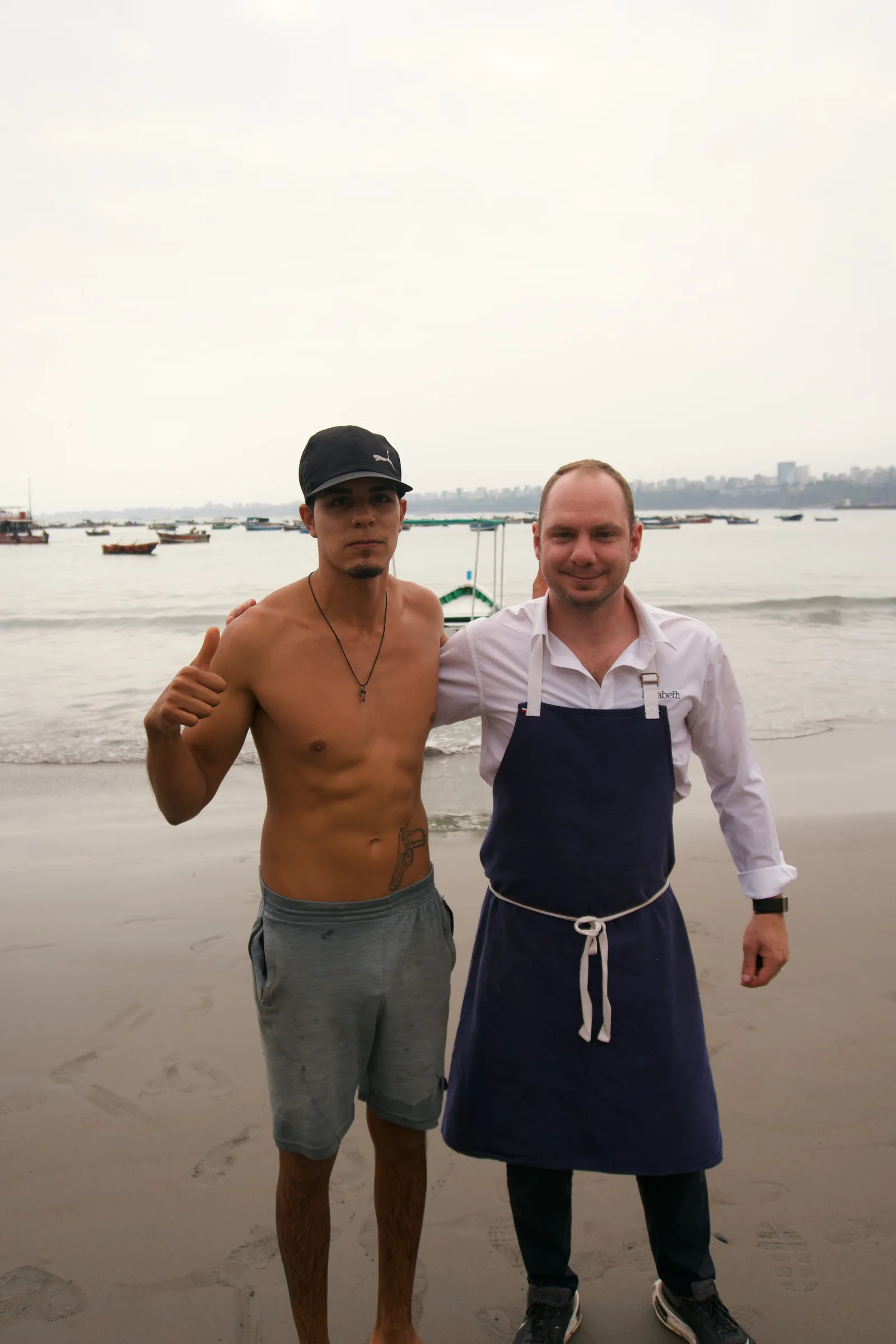 Jason in his apron standing beside a man on a beach in Peru