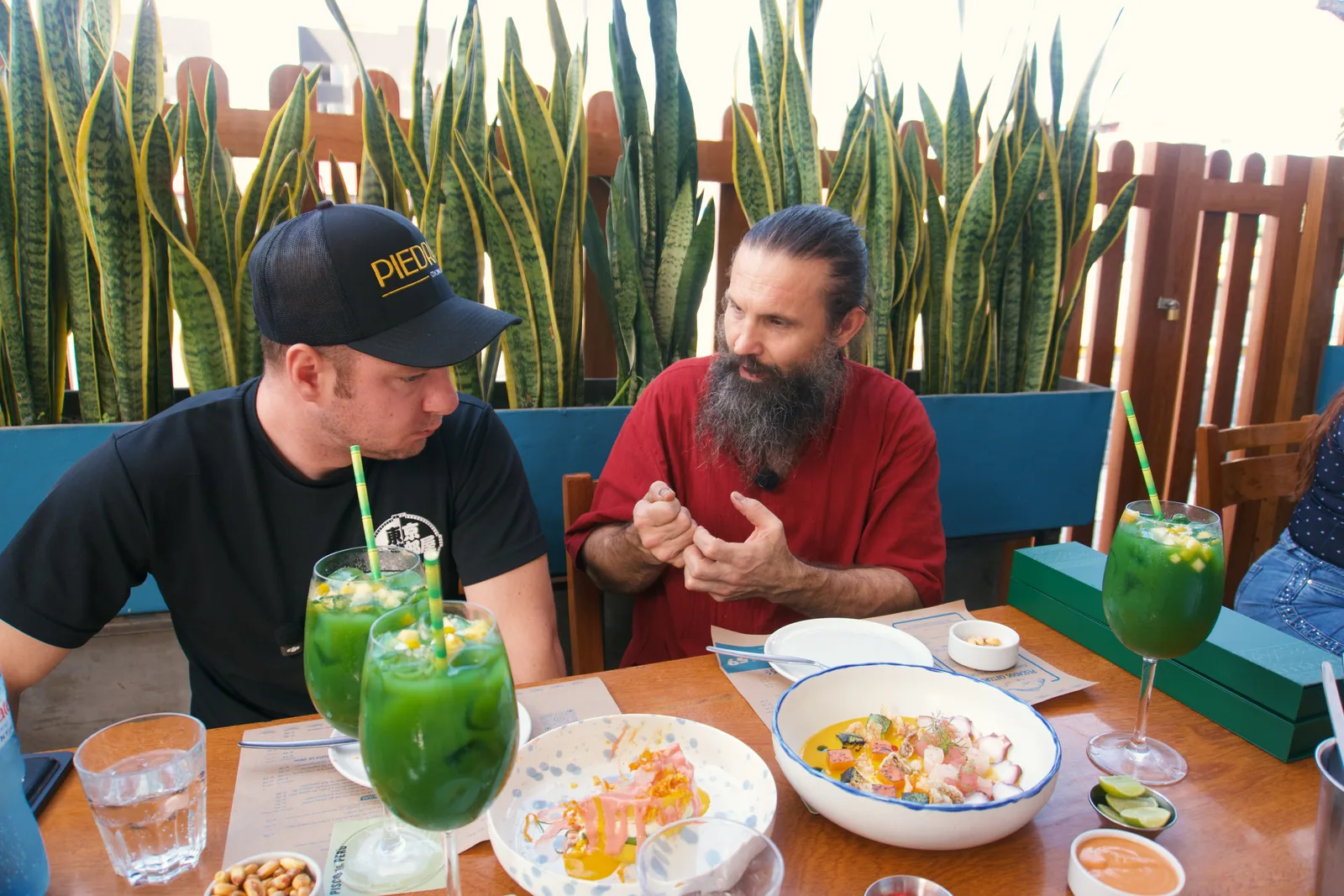 Jason and a man talking over plates of food and green drinks in Peru
