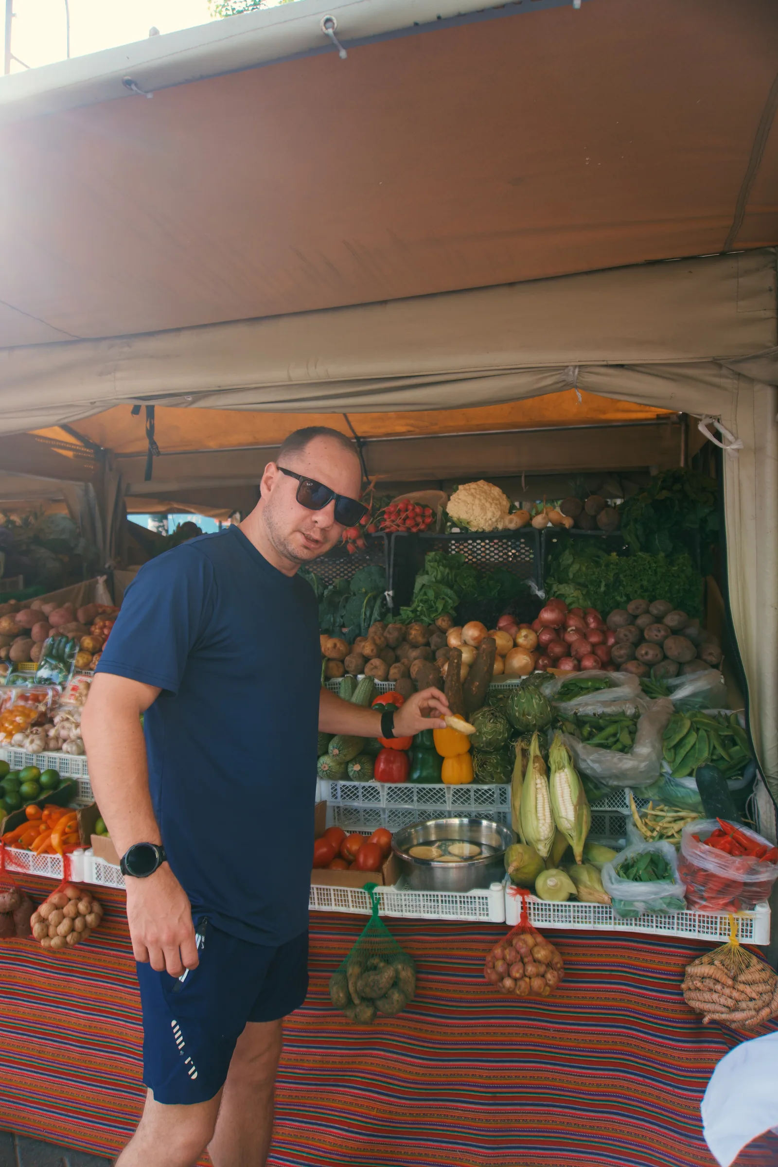Jason beside a produce stall stacked with fruit and vegetables in Peru