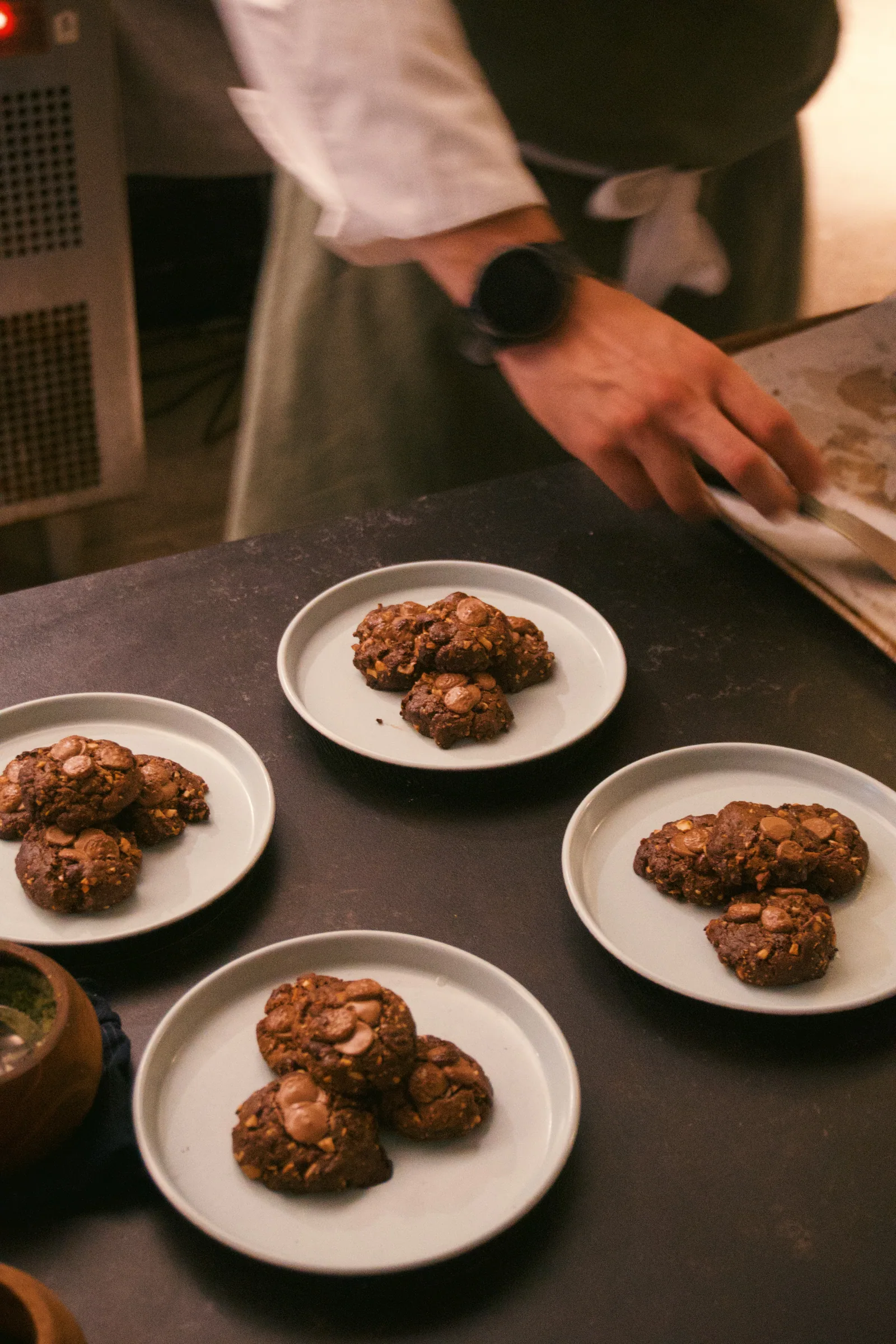 Plates of cookies beside a cook’s hands at the kitchen pass