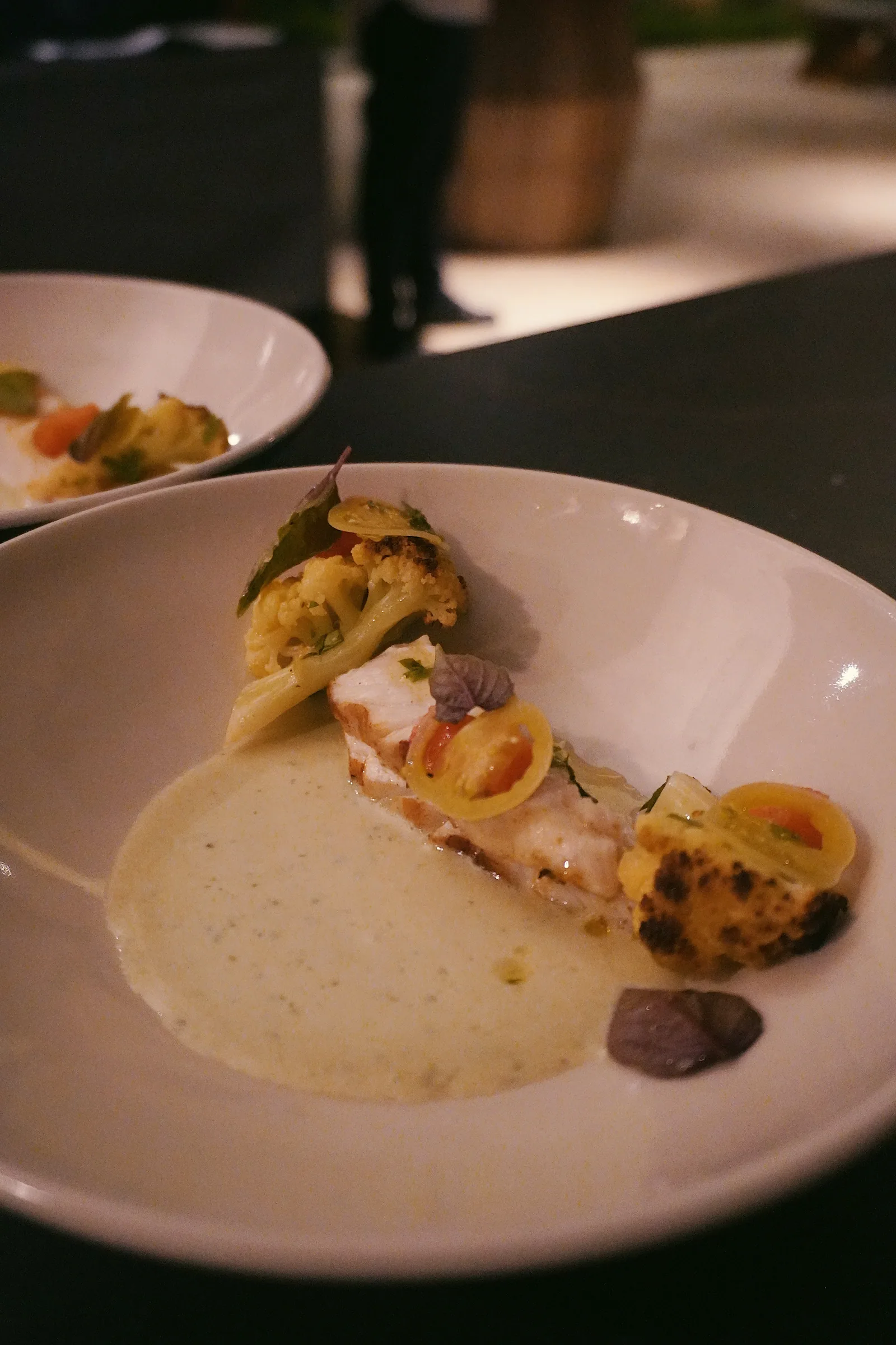 A plated dish with sauce, vegetables and herbs at Cap Karoso