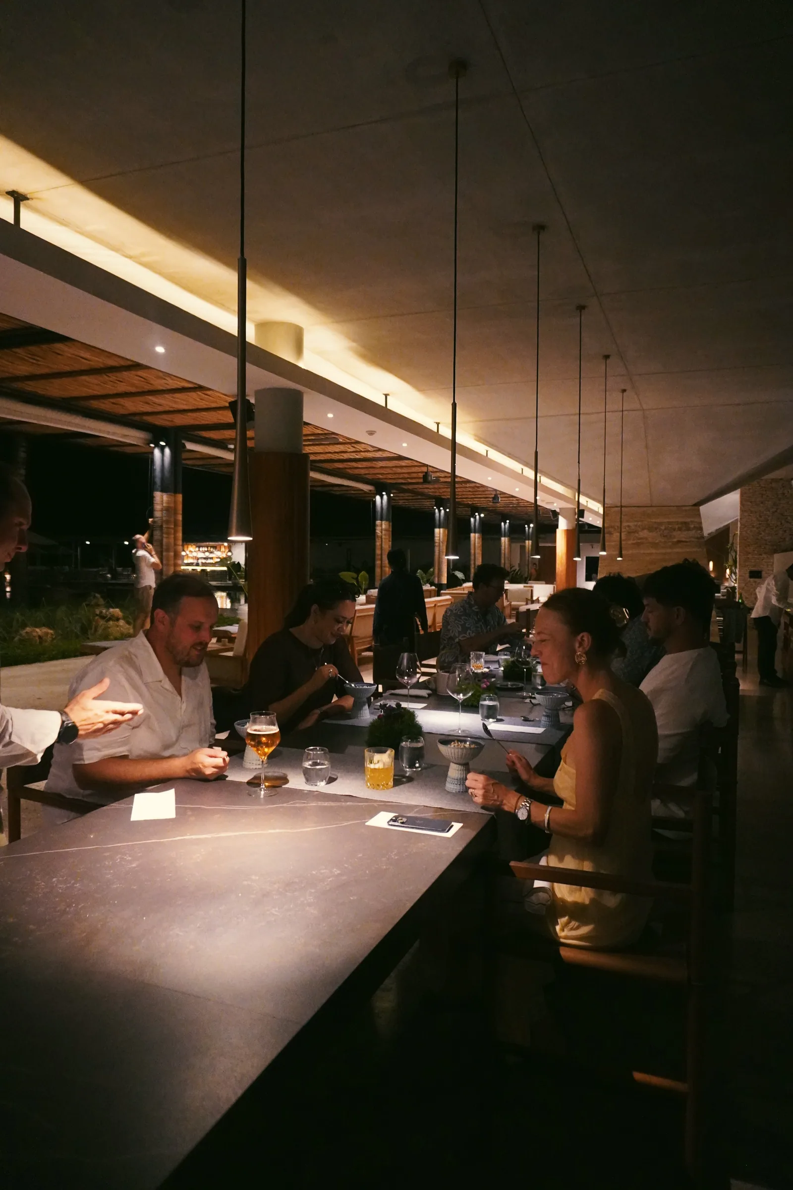 Guests eating at a long counter beneath pendant lights at Cap Karoso