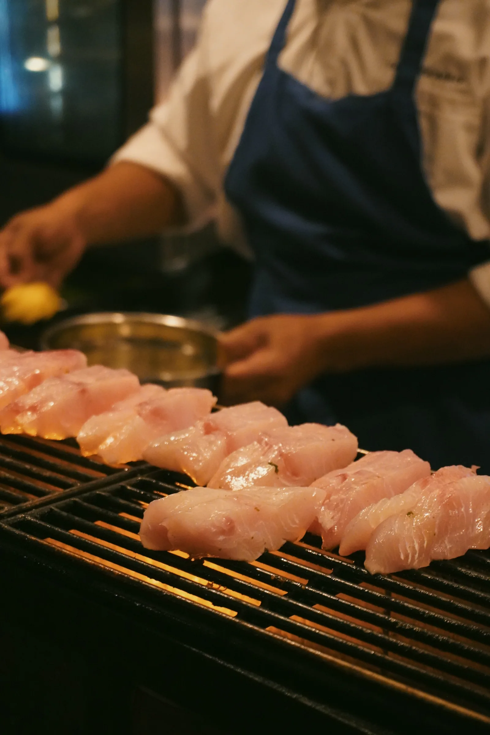 A cook preparing pieces of fish on a wire rack in the Sumba kitchen